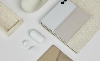 El estuche de carga blanco cerrado que se muestra sobre un escritorio mirando hacia abajo con los audífonos blancos y un teléfono celular blanco