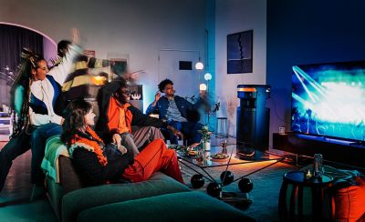 Young people at home watching a concert on television and using the ULT TOWER 10 speaker to provide the sound.