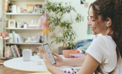 A young woman sat at a table with her phone in her hands while wearing LinkBuds Fit.