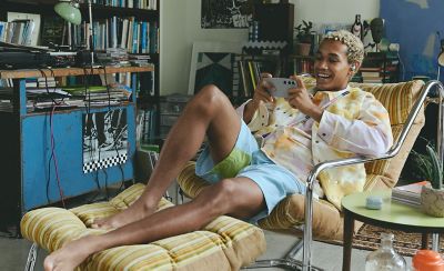 A young man wearing LinkBuds Fit reclining in a chair watching something on his smartphone.