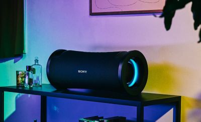 The ULT FIELD 7 portable speaker on a table in a living room with multi-coloured illumination.