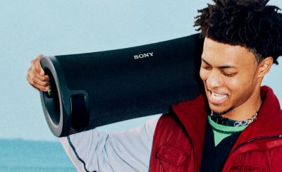 Close- up of a young person walking along a beach with the ULT FIELD 7 portable speaker on their shoulder.
