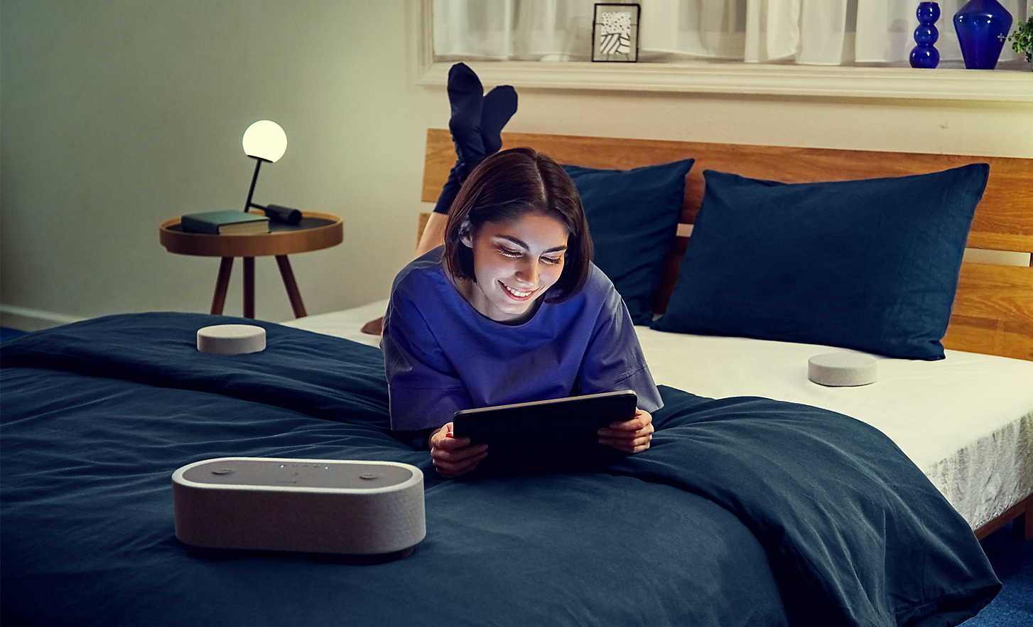Image of a person lying on a bed watching a tablet, surrounded by the three HT-AX7 speakers