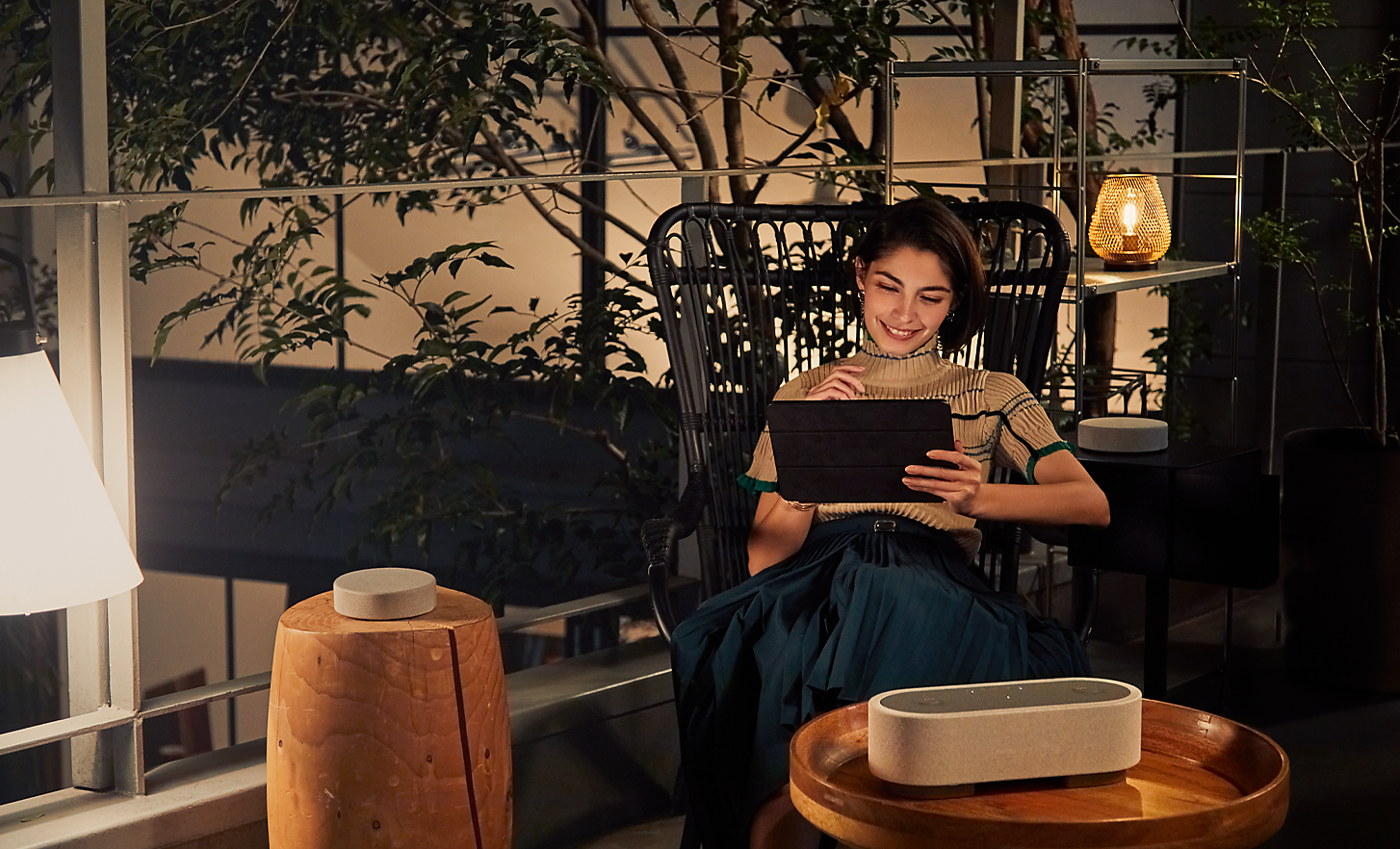 Obrázok osoby sediacej na kresle, ktorá sa pozerá na tablet a je obklopená tromi reproduktormi HT-AX7