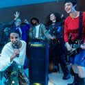 Una persona cantando en un micrófono al lado del TOWER 9AC con amigos a su alrededor cantando y tocando una guitarra.