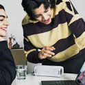 Two people making a video call on a laptop with an ULT FIELD 1 portable speaker providing the audio.
