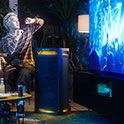 Un grupo de personas mirando y disfrutando de un concierto en un televisor con la música reproduciéndose a través del parlante TOWER 9AC