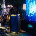 A group of people watching and enjoying a concert on a TV with the music being played through the TOWER 9 speaker