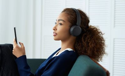 Mladá žena s černými bezdrátovými sluchátky Sony WH-CH530 odpočívající v interiéru