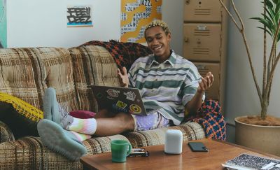 A young man sat on a sofa with a LinkBuds Speaker on a coffee table in the foreground.