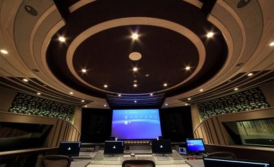 Estudio de sonido con una pantalla grande, cuatro pantallas pequeñas y una mesa de mezclas