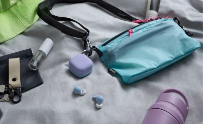 A personalised set of LinkBuds Open earbuds and their accompanying charging case on a bed with an array of personal items around them.