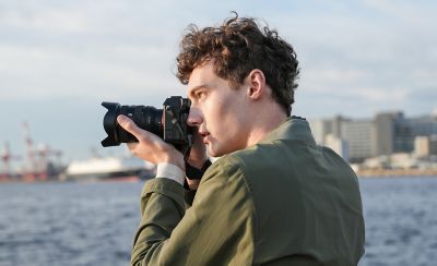 Man shooting in coastal location with camera hand-held, using viewfinder