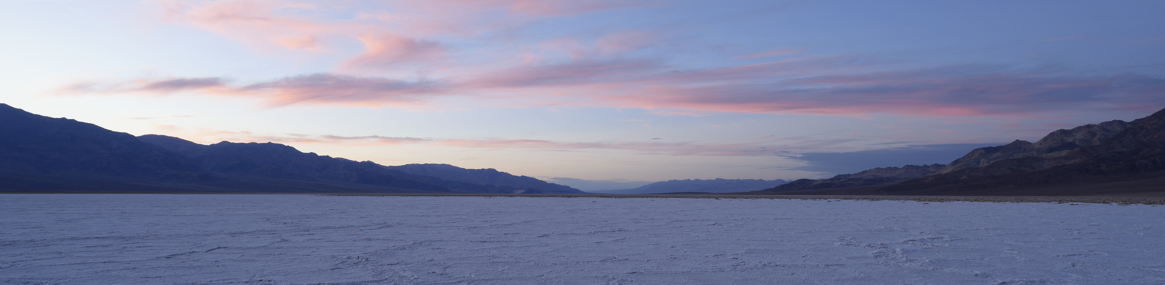 Vidvinkelbilde av øde landskap og solnedgang bak fjerne fjell