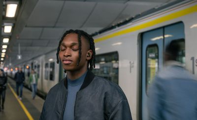 Image of a person with eyes closed, standing on a train platform wearing the WF-1000XM5 Headphone