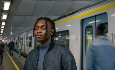  Image of a person with eyes closed, standing on a train platform wearing the WF-1000XM5 Headphone