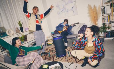 A woman sings into a microphone and a man is playing a guitar, both plugged into an SRS-XV800, whilst their friends dance