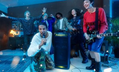 A person singing into the ULTMIC1 next to the TOWER 9 speaker with their friend playing a guitar and the other friends singing in the background