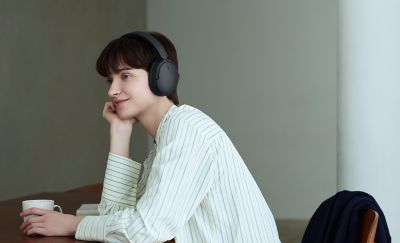 Žena s černými sluchátky Sony WH-CH730N odpočívající u stolu v interiéru