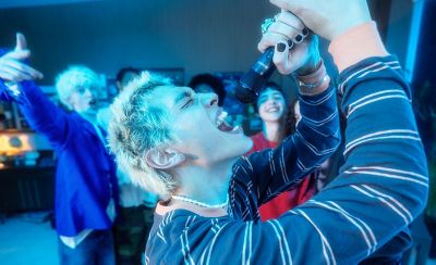 Una persona cantando con el ULTMIC1 y sus amigos mirando en el fondo.