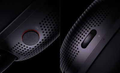 Primer plano del control de volumen y el botón de silencio en los laterales de los audífonos tipo diadema negros sobre un fondo negro