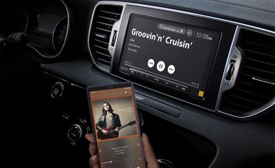 Internal view of a car dashboard showing the XAV-9000ES media receiver paired to a smartphone. 