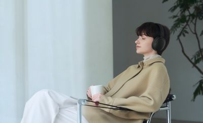 O femeie relaxându-se în fotoliu, purtând o pereche de căști Sony WH-CH730N, modelul negru
