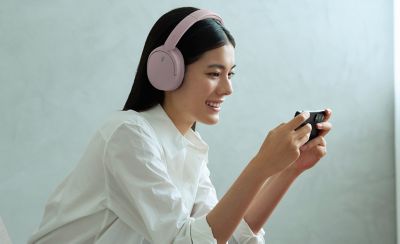 O femeie purtând o pereche căști Sony WH-CH730N, modelul roz, folosind smartphone-ul acasă