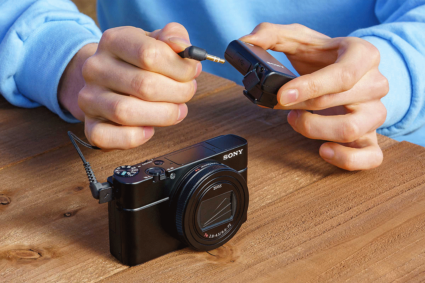 A person connecting the ECM-W2BT with a cable to a compatible camera via a 3.5 mm stereo mini-jack