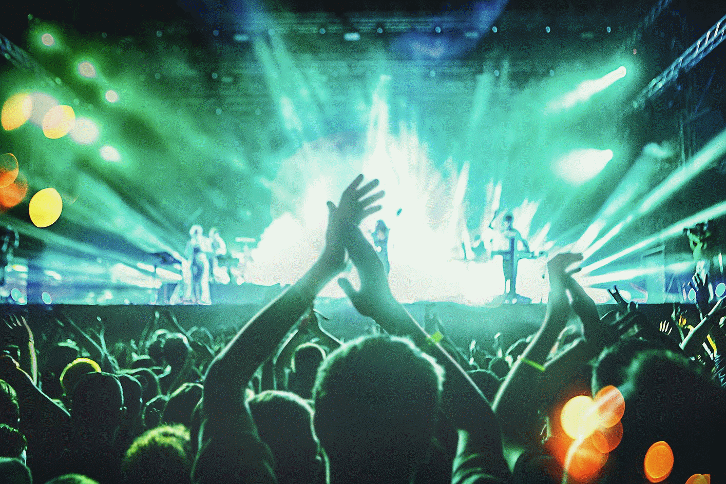 Zdjęcie z koncertu na żywo z wieloma klaszczącymi osobami i niebiesko-zielonym oświetleniem