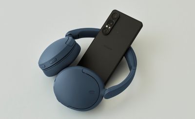 Căști Sony WH-CH730N, modelul albastru, așezate lângă un smartphone