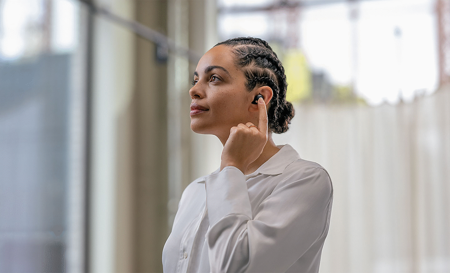 Kuva WF-1000XM5-kuulokkeita pitävästä henkilöstä, joka napauttaa kuulokkeita sormella