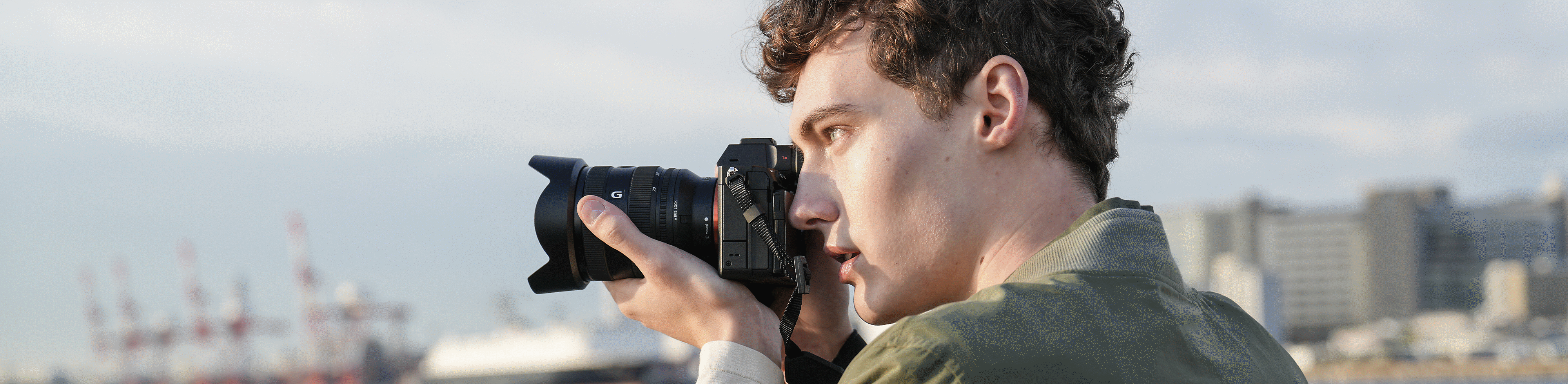 Homem a captar manualmente com a câmara num local costeiro, usando o visor eletrónico