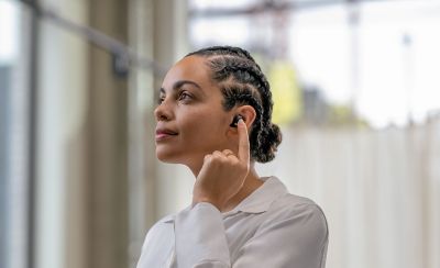 Image of a person wearing the WF-1000XM5 headphones and tapping them with one finger