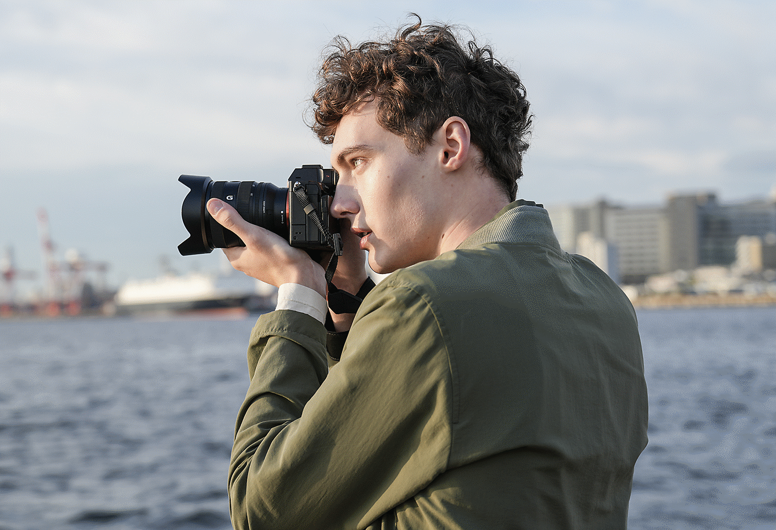 Žmogus fotografuoja pakrantėje, laikydamas fotoaparatą rankose ir naudodamas vaizdo ieškiklį