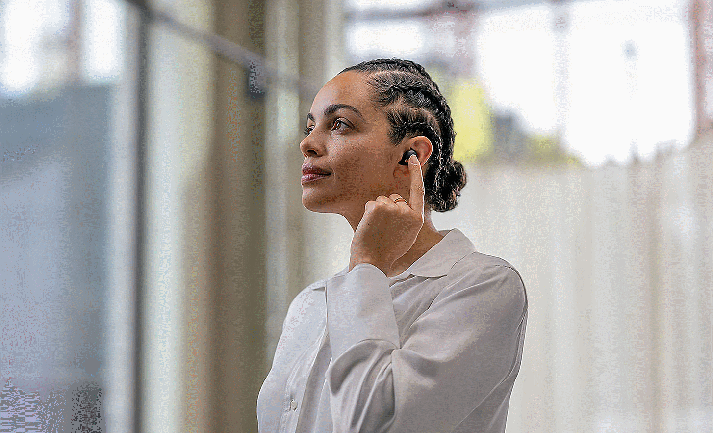 WF-1000XM5 fülhallgatót viselő személy képe, aki egy ujjal koppint a fülhallgatóra