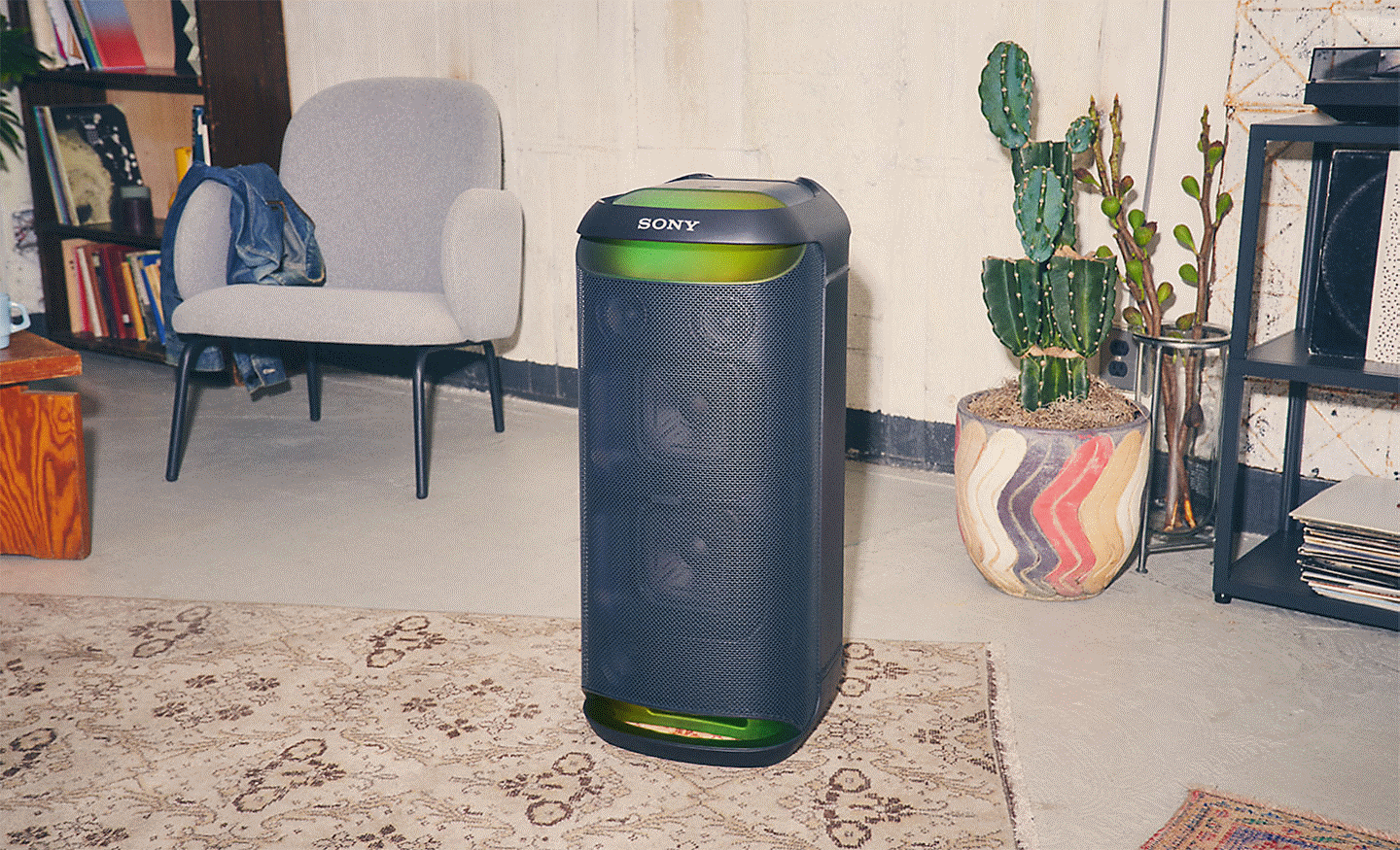 Image of the SRS-XV800 speaker with green ambient lightning sitting on a rug in a room with a chair and a cactus