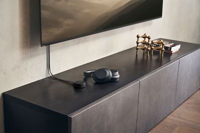 Image of headphones on a media unit, next to the Sony WLA-NS7 wireless transmitter connected to a BRAVIA TV