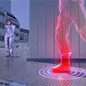 A person holding a plastic gun in a computer game world aiming at a 3D model with rings around the foot for sound