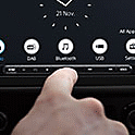 Image of the XAV-AX4050 in a dashboard with a clock and multiple buttons on-screen and a finger hovering in front 