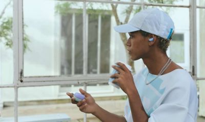 A young man in a white baseball cap and a white jumper wearing a pair of LinkBuds Fit earbuds.