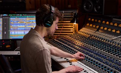  Lydtekniker som justerer spaker på et miksebord i et studio. Han bruker MDR-M1-monitorhodetelefonene mens han mikser lyden.