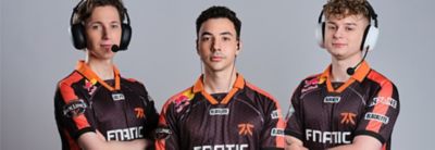 Three gamers wearing shirts with the Fnatic logo on the front. Two are wearing over ear headsets with mics, one is wearing in-ear wired headphones.
