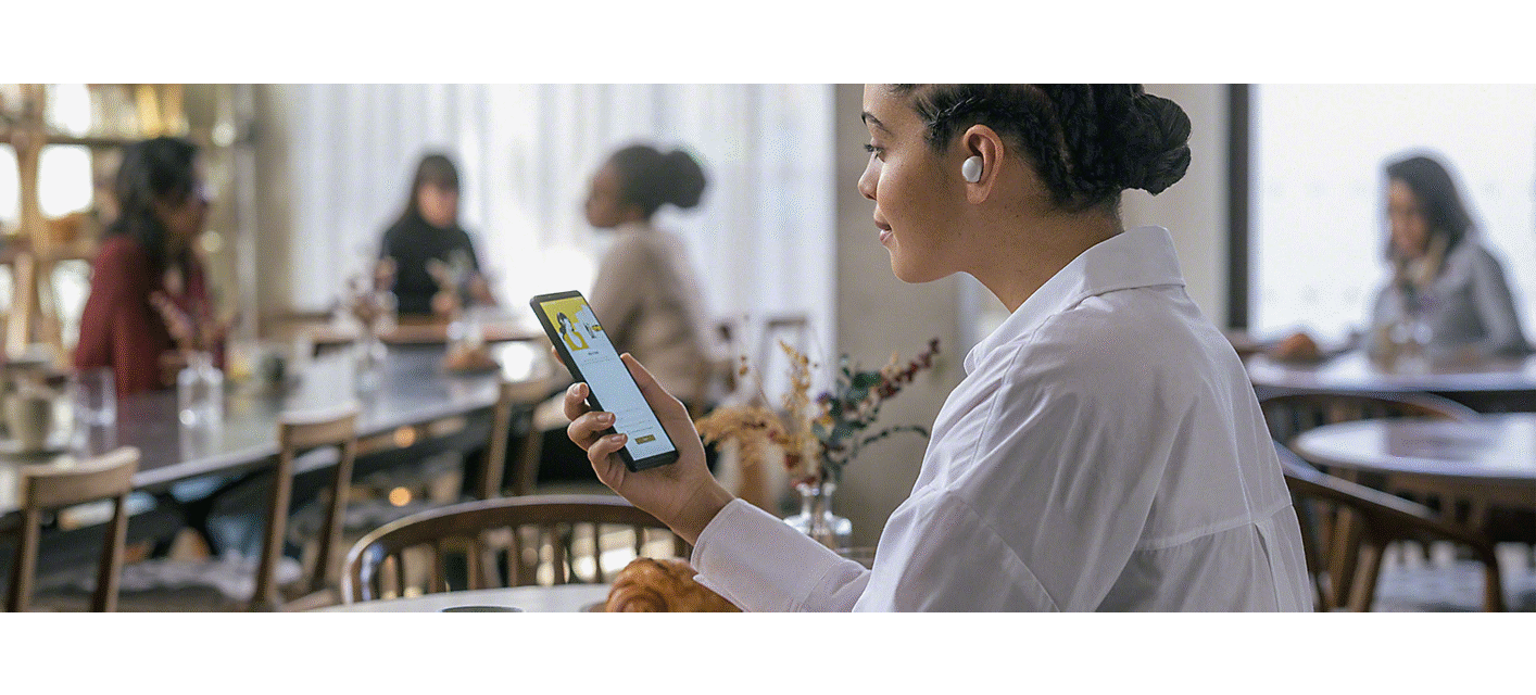 Image a person in a coffee shop using an Xperia phone and listening to a pair of Sony in-ear headphones