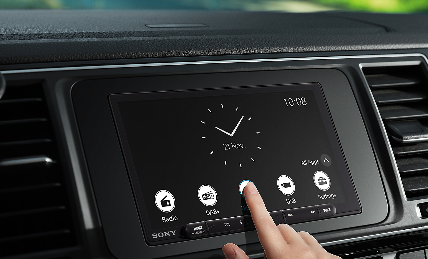 Image of the XAV-AX6050 in a dashboard with a person touching the screen with one finger