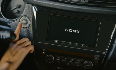 Afbeelding van de XAV-AX6050 in een dashboard met een Sony-logo op het scherm en een persoon die de motor van de auto start