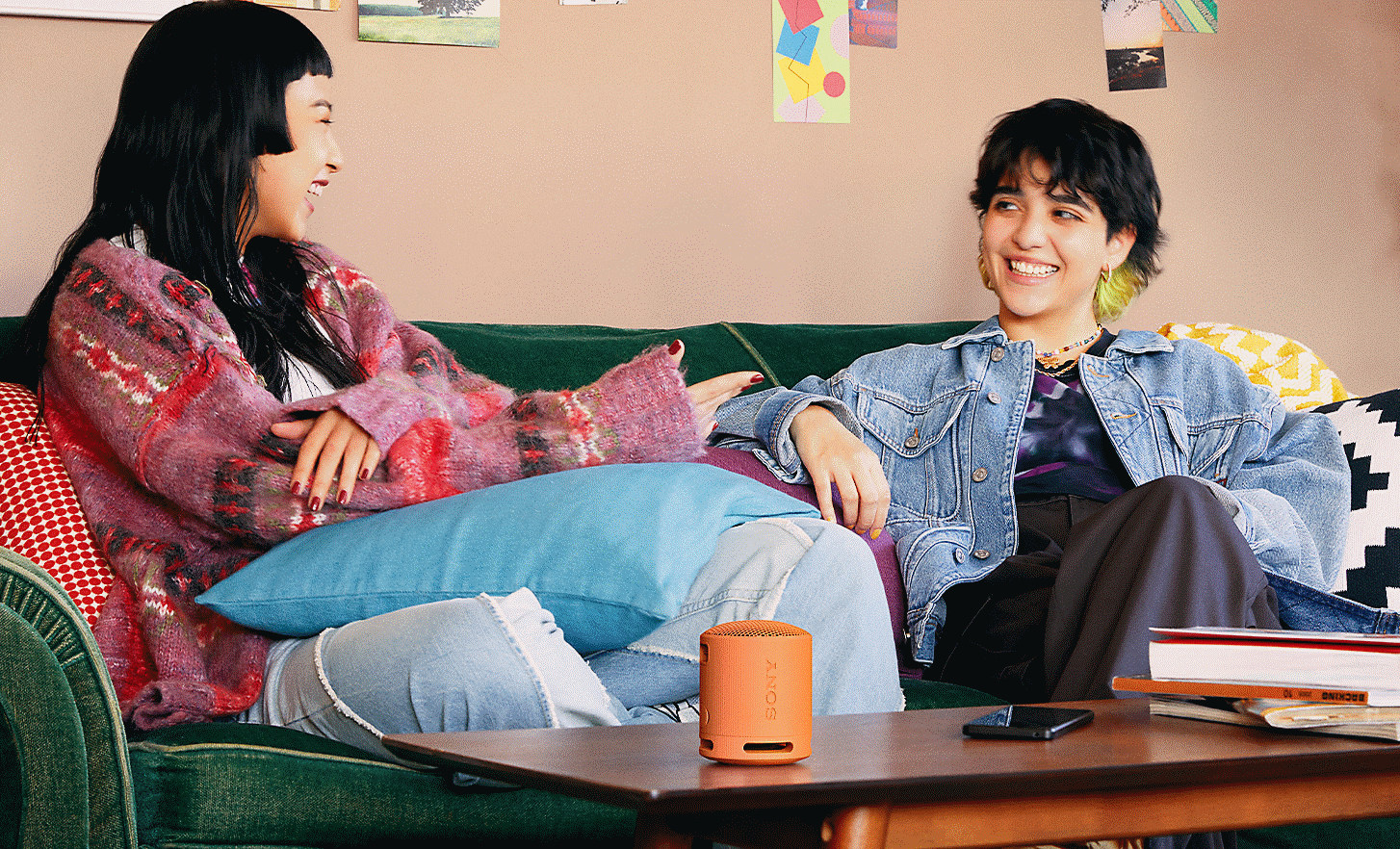 Image of two people smiling whilst sitting on a sofa with an orange SRS-XB100 speaker on the coffee table in front of them
