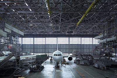 Gambar yang menunjukkan ruang interior hanggar besar tempat pemeliharaan pesawat, dengan setiap detail tampak jelas, termasuk struktur baja yang rumit.