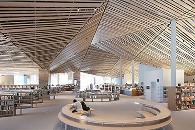 Image of the interior space of a large library with an elaborate design using many straight wood planks on the ceiling, with resolution to every corner of the screen