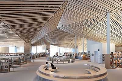Gambar ruang interior perpustakaan besar dengan desain rumit menggunakan banyak papan kayu lurus di langit-langit, dengan resolusi di setiap sudut layar